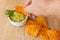 Man`s hand taken a nacho and scooping up some guacamole sauce to taste. Mexican ethnic food concept