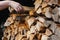 A man`s hand takes a birch dry chipped log from a woodpile