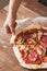 A man`s hand takes a piece of pizza with tomato paste, cheese, salami and basil