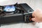 A man`s hand turns on a portable gas stove on a wooden table. An alternative source for cooking at home during a power outage