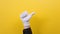 A man\'s hand in a white glove shows a thumbs-up gesture. Yellow background. Close up. Positive gestures