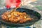 Man`s hand with wooden turner mixing fried chicken meat with tomato sauce in large flat pan. Preparing paella or jambalaya