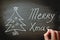 Man`s Hand Writing Merry Christmas on Blackboard with Chalk. Doodle Christmas Tree New Year