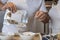 Man's hands emptying granola into a white bowl in a kitchen