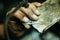 Man`s hands goldsmith work on a piece of silver with a metal saw on the work table, close up, selected focus