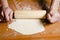 Man\'s hands rolled dough with wooden rolling pin on the wooden table.
