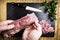 Man`s hands splitting a pork tenderloin with a knife next to some parsley branches on a black slate griddle