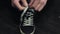 Man\'s hands tie white laces on right sport shoe.