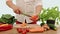 The man\'s hands using a kitchen knife cutting the sweet peppers on the wooden cutting panel.