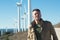 Man`s portrait outdoor against blue sky with wind turbine. Windmill generators.