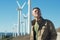 Man`s portrait outdoor against blue sky with wind turbine. Windmill generators.