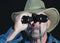 A Man in a Safari Hat Looks Through Binoculars