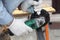 A man in the safety gloves is cutting metal using a green angle grinder tool with sparks on a work bench. Horizontal