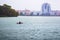 A man sailing on a boat canoe on a river in a rainy weather against the background of modern city buildings_