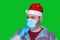 Man in a Santa Claus costume and a medical mask. isolated on a green background. Bad Santa represents a bad year