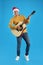 Man in Santa hat playing acoustic guitar on light blue background. Christmas music