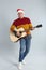 Man in Santa hat playing acoustic guitar on light grey background. Christmas music