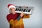 Man in Santa hat playing synthesizer on light grey background. Christmas music