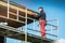 Man on scaffolding installing new wooden planks on house roof eaves
