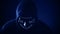 Man in scary lighting neon glow mask in hood in Phantom Blue color. Halloween and horror concept