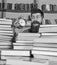 Man, scientist peeking out of piles of books with alarm clock. Teacher or student with beard studying in library. Time