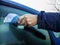 A man scrapes hoarfrost with a plastic scraper from the side window of a blue car. Hand without gloves in the cold