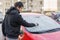 Man is scraping ice from frozen windshield window of car in winter