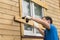 A man with a screwdriver in his hand is blocking the windows of the house with boards, side view