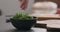 Man seasoning fresh salad with radish, cucumber and herbs in black bowl