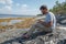 man is seating on the stone near of the sea and working with laptop