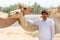 Man selling hay stacks on the side of the road near Al Ain posing with the camels