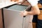 A man or service worker in special clothing installs, disassembles or tries on a built-in dishwasher in a niche of kitchen