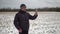 Man in a shabby winter jacket having an online video chat standing in a rural field in winter