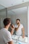 Man shaving using electric shaver trimming his beard in home bathroom- morning grooming routine people concept. Young