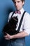 Man in shirt, suspender and pink bow tie holding cute black cat and looking at camera on blue background