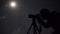 Man shooting the night cloudy sky under moon with a tripod