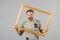 Man shout with picture frame on grey background. Angry macho with beard hold wooden photo frame. Guy with empty framework. Creativ