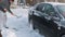 A man with a shovel clears snow around a car