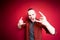 A man shows the Hook& x27;em horns gesture and shouts loudly against a red background in the studio. Rock music concept