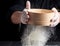 Man sifts white wheat flour through a wooden sieve