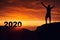 Man silhouette on the mountain top watching the sunrise and 2020 years while celebrating