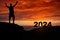 Man silhouette on the mountain top watching the sunrise and 2024 years while celebrating