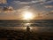 Man silhouette by sea on sandy beach at sunset.