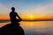 Man silhouette sitting on stone at the seaside contemplating sun