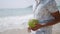 Man sips fresh coconut on tropical beach, sea waves in background. Relaxed male enjoys natural drink, beach lifestyle