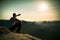 Man sit on rock edge. Hiker makes shadow with hand and watch to colorful mist in forest valley.