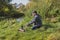 Man sits alone with a cup of coffee on the river bank near the fire. Rest at nature. Man sits alone near a campfire by the river