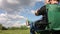 A man sits in a camping chair and speaks on the phone. Meadow with green grass. Blue sky with clouds