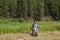 A man sits on a chair in a field against the background of a coniferous forest in his hand holding a machete next to a shovel