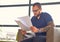 A man sits on a chair and reads a document.